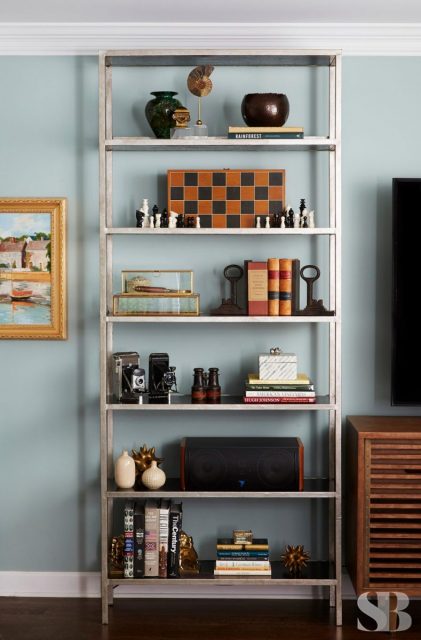 bookcase against a blue wall with a chess b oard and other various objects