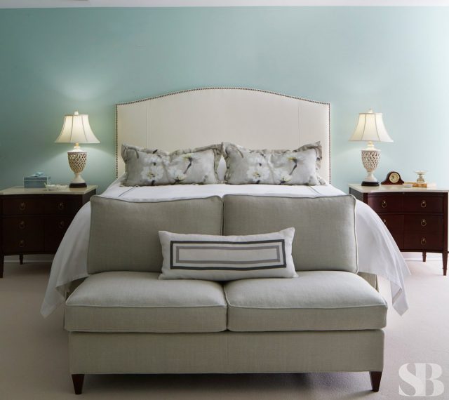 master bedroom with upholstered headboard and bench against light blue walls