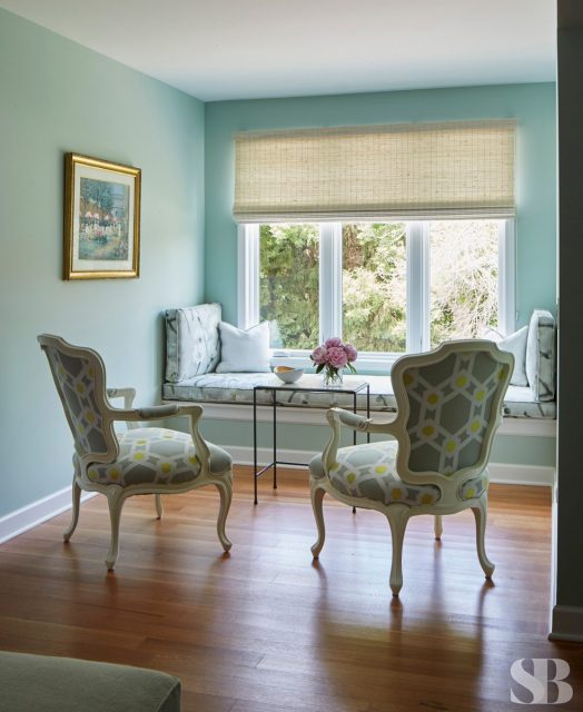 upholstered window bench and two chairs in a small seating area with light blue walls