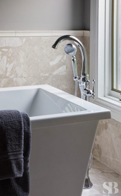 square white bathtub with stainless steel faucet against marble tile
